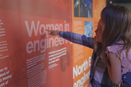 A photo of two children pointing at a red exhibition board, which reads 'Women in engineering'.