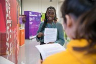 teenage girl of colour wearing a green jumper holding worksheet up to camera