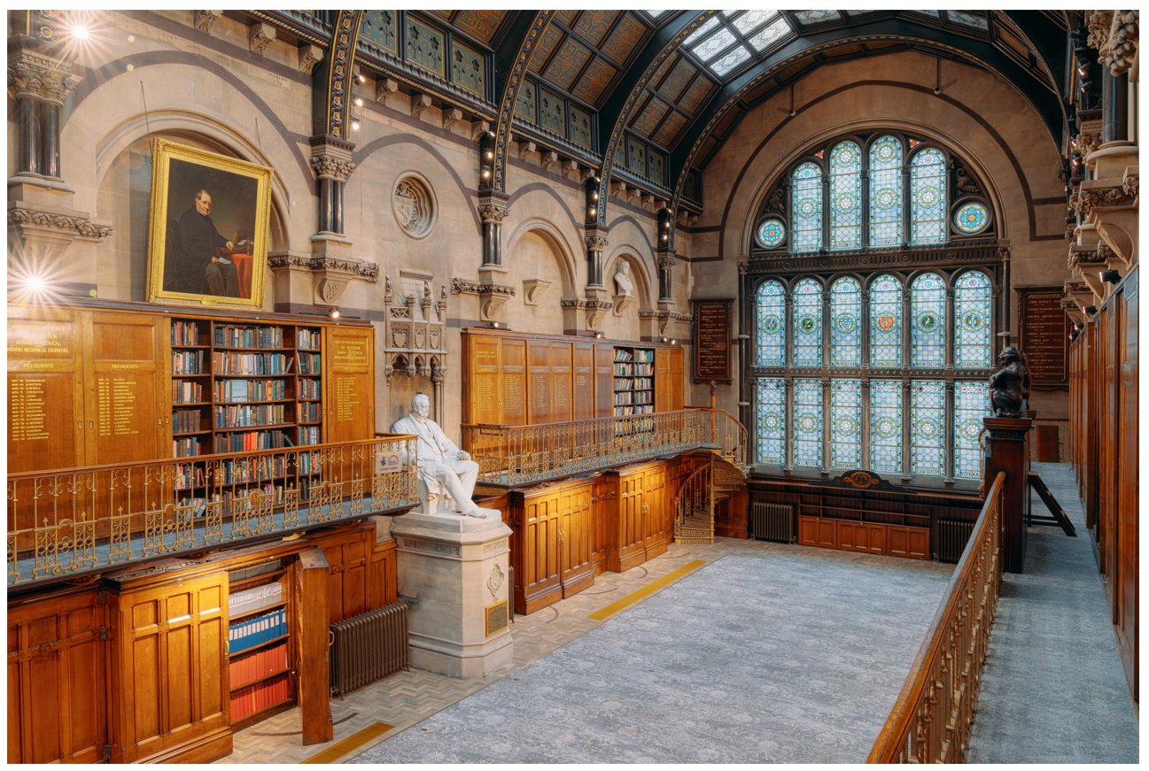 A photo of The Common Room's Wood Hall. Wide lens shot from the balcony. A large stained glass window is in the background, and wooden bookcases and panels, plus long golden balconies, line the room down towards the window. In the centre of the shot, half way down the room, is a large statue of Nicholas Wood on a plinth - the Hall's namesake.