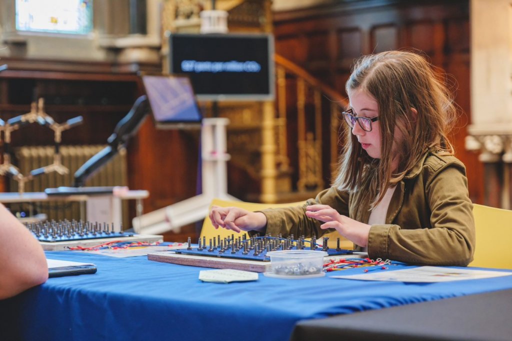 Girl doing an engineering dexterity activity using a board, and some wires, nuts and bolts