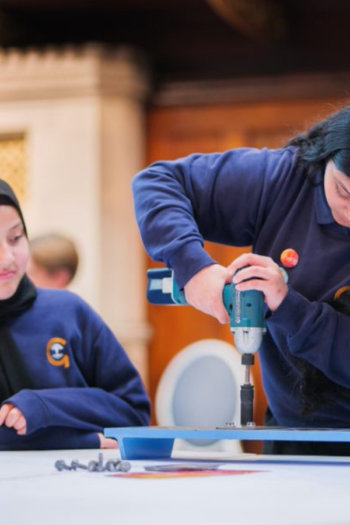 Two girls visiting The Common Room, one practices using a drill whilst the other watches